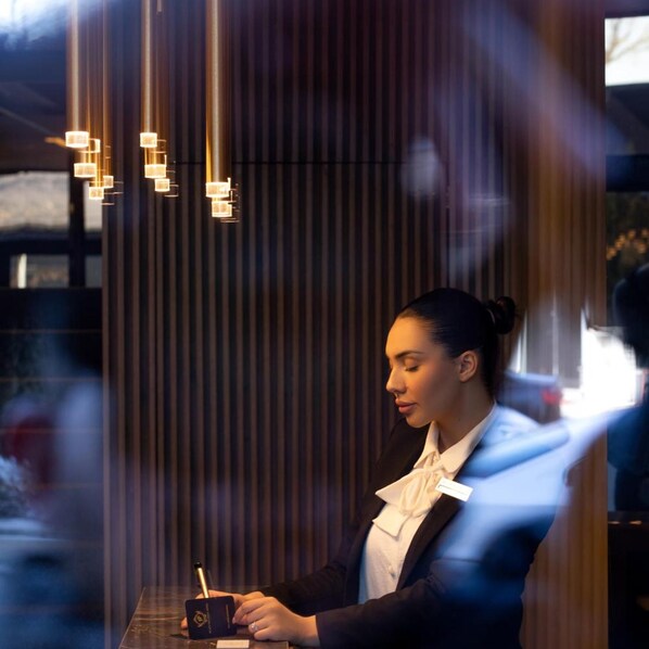A person seated at a table with a drink, in a room with vertical wooden slats and hanging pendant lights. - Plaza Boutique Hotel Prishtina (Pristina)