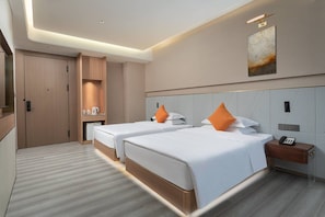 A hotel room with two beds, a bedside table with a phone, a wall-mounted artwork, and a wooden wardrobe.