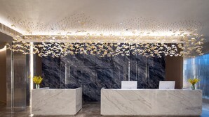 A reception area with marble counters, a decorative ceiling, and a stone wall backdrop. - Hawthorn by Wyndham Honghe Mile Hot Spring (Honghe)