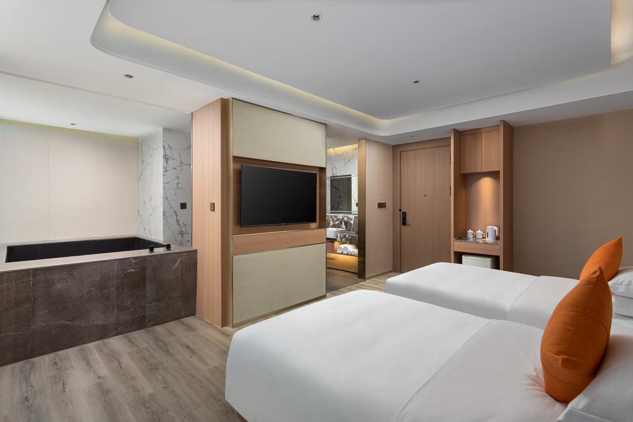 A modern hotel room with a flat-screen TV, a bathtub, and two beds with pillows.