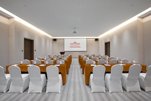 A conference room with rows of tables and chairs, a projector screen, and a podium.
