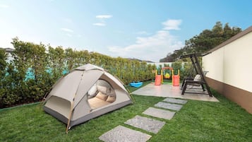 A tent set up on a grassy area with stepping stones, a swing set, and a slide in the background.