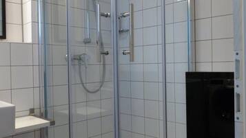 Eine Duschkabine mit Glaswänden, einer Handbrause und einem am Wand montierten Wasserhahn.
