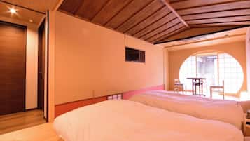 A bedroom with two beds, a wooden ceiling, a small window, and a view of the outside.