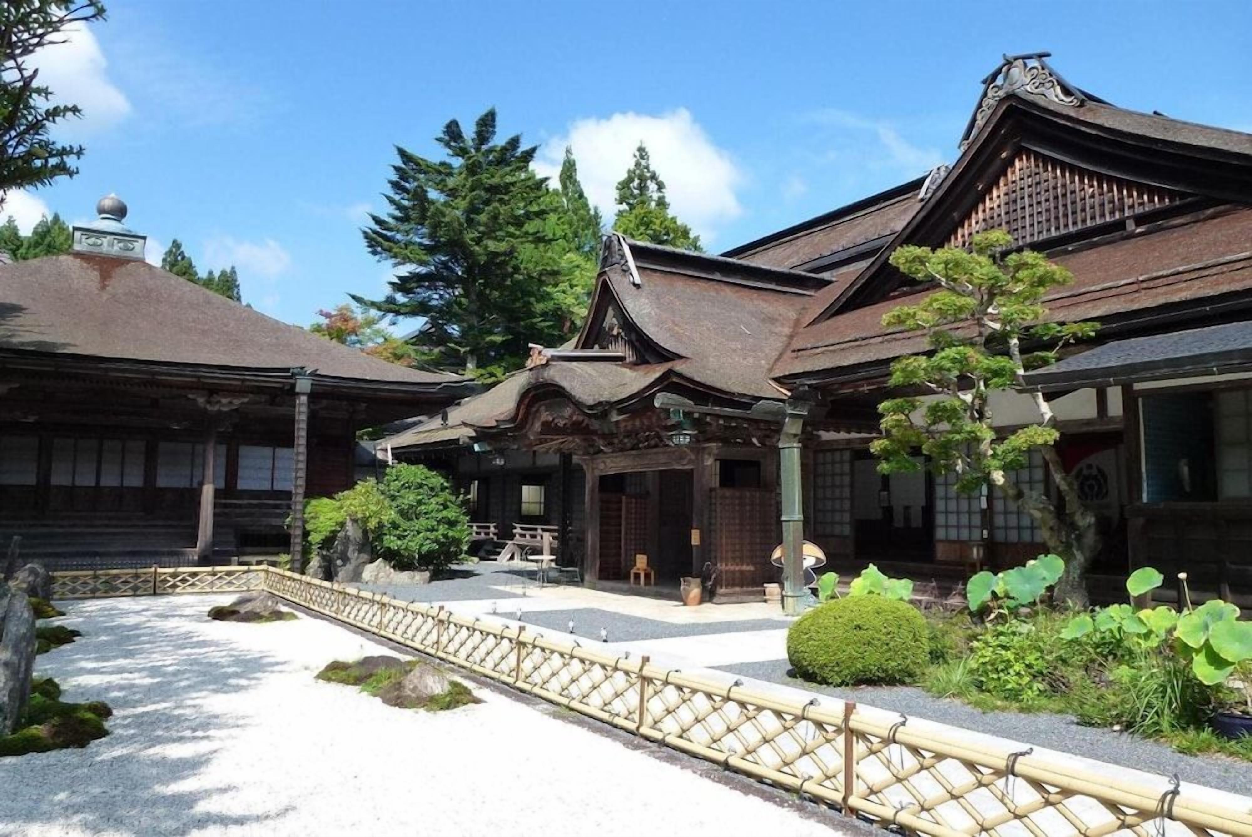 A traditional Japanese building with a wooden structure, a tiled roof, and a gravel courtyard with a bamboo fence.
