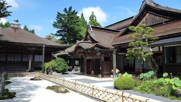 A traditional Japanese building with a wooden structure, a tiled roof, and a gravel courtyard with a bamboo fence.