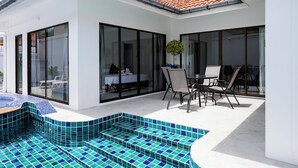 Et moderne hus med swimmingpool, glasdøre og en terrasse med udendørs møbler.