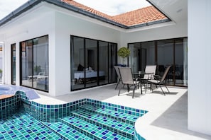 Una casa moderna con piscina, puertas de vidrio y un patio con mobiliario exterior.