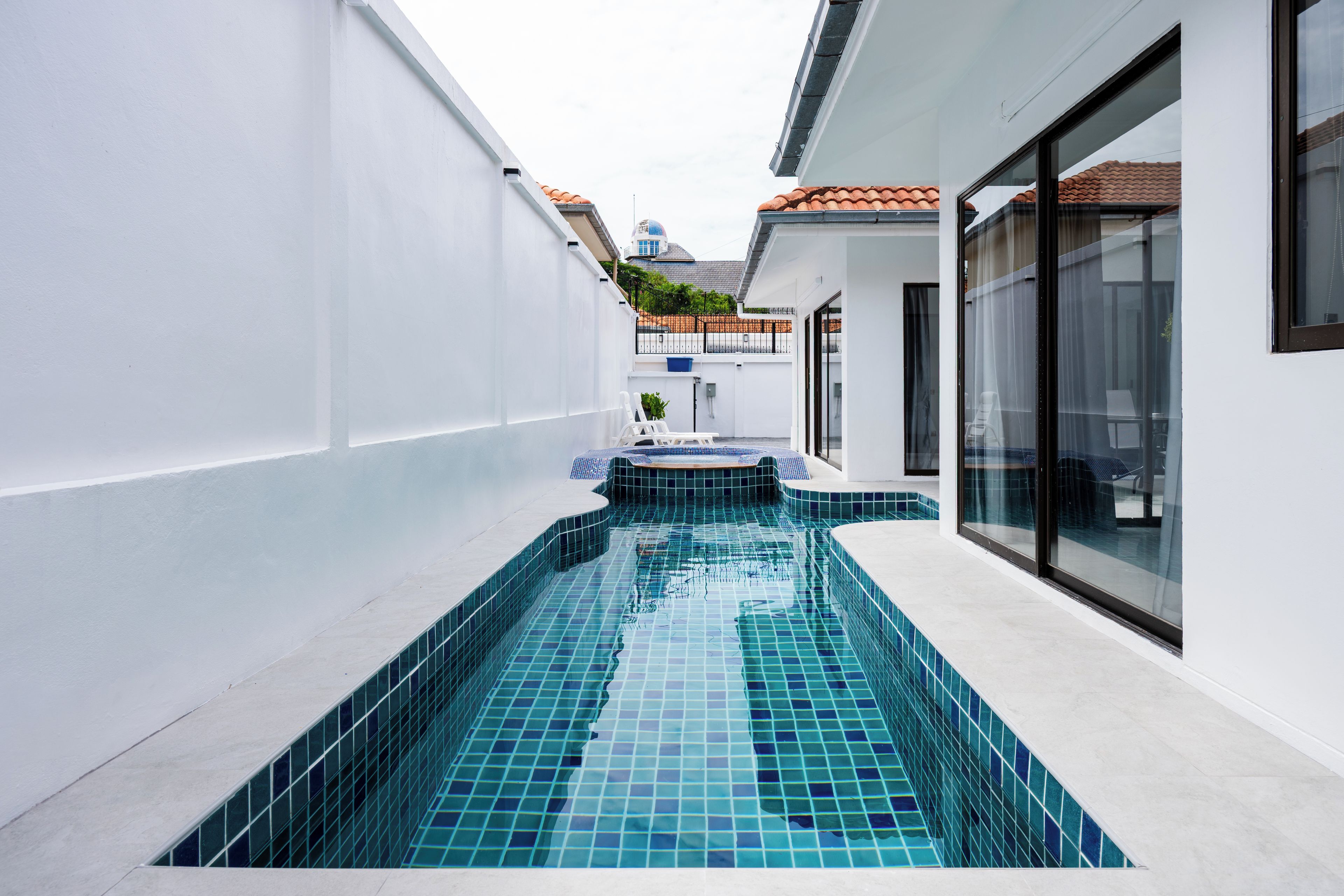 A swimming pool with blue tiles, surrounded by white walls and a glass door.