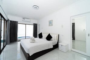 Una habitación de hotel moderna con una cama grande, una mesita de noche pequeña, un armario y vista al mar.