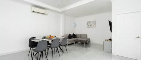 A modern dining area with a table set for four, a sofa, and a television on a stand.