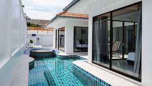 En moderne udendørs swimmingpool med fliset gulv, et overdækket opholdsområde og et glasindrammet rum med en seng.