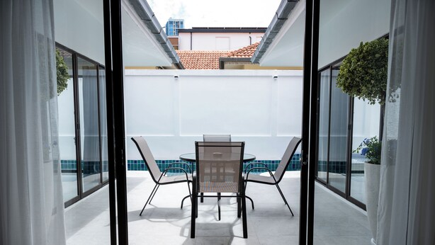 Udsigt gennem et glasdør til en patio med et bord og stole, flisegulv og en bygning med et flis tag i baggrunden.