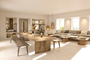 Een ruime woonkamer met een grote houten salontafel, een bank en een eettafel.