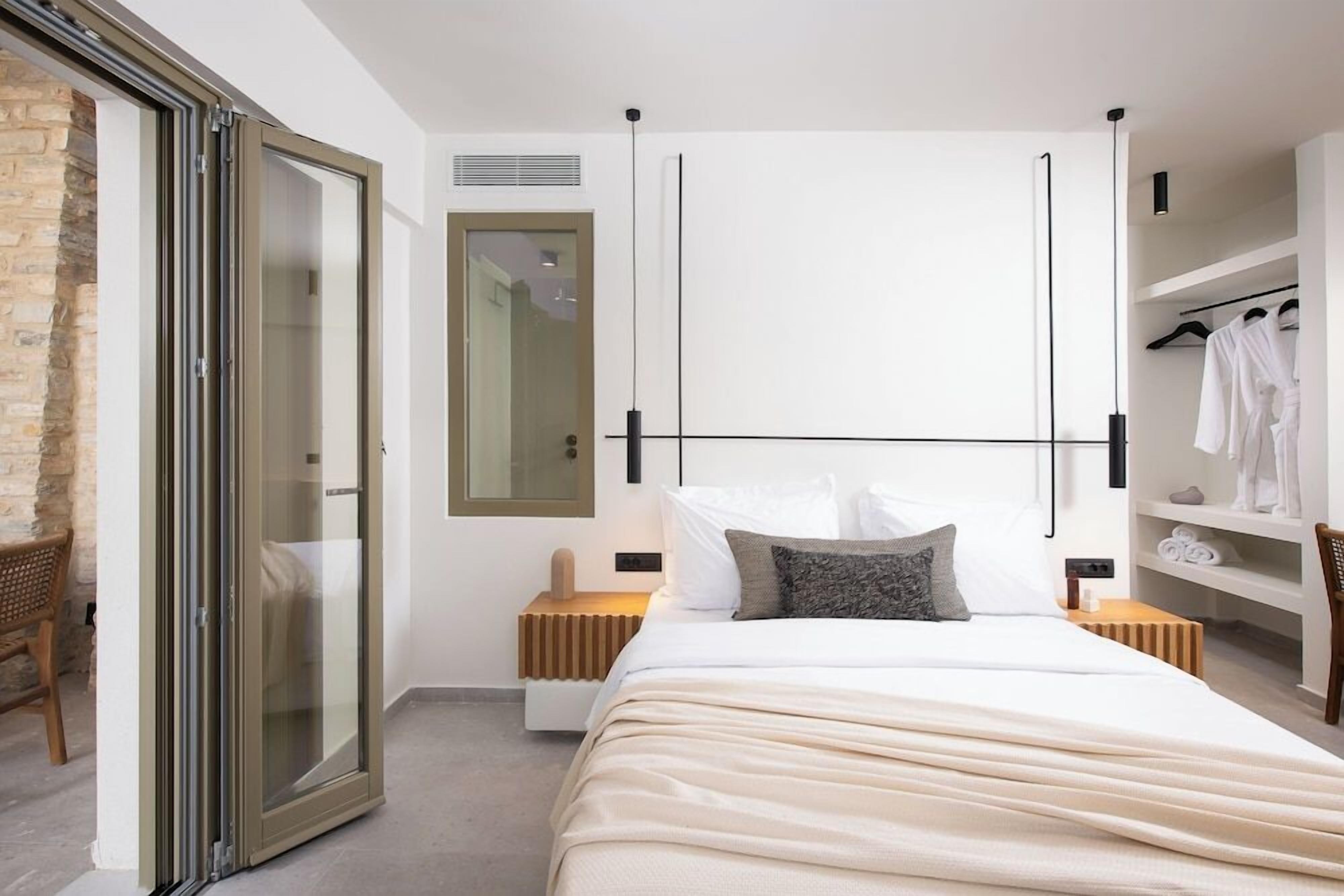 Une chambre moderne avec un grand lit, une porte-fenêtre coulissante, une armoire intégrée et un coin salon avec un fauteuil.