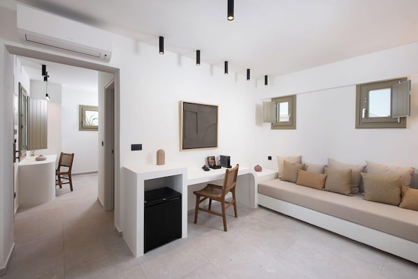 Un interior moderno con un escritorio blanco, un bote de basura negro, un sofá beige y un espejo montado en la pared.