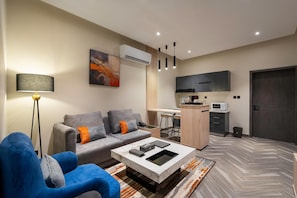 A modern living room with a sofa, a coffee table, and a lamp. There is a kitchen area with a microwave and a sink. - Gardn Millennium Al-salamah Hotel Jeddah (Jeddah)