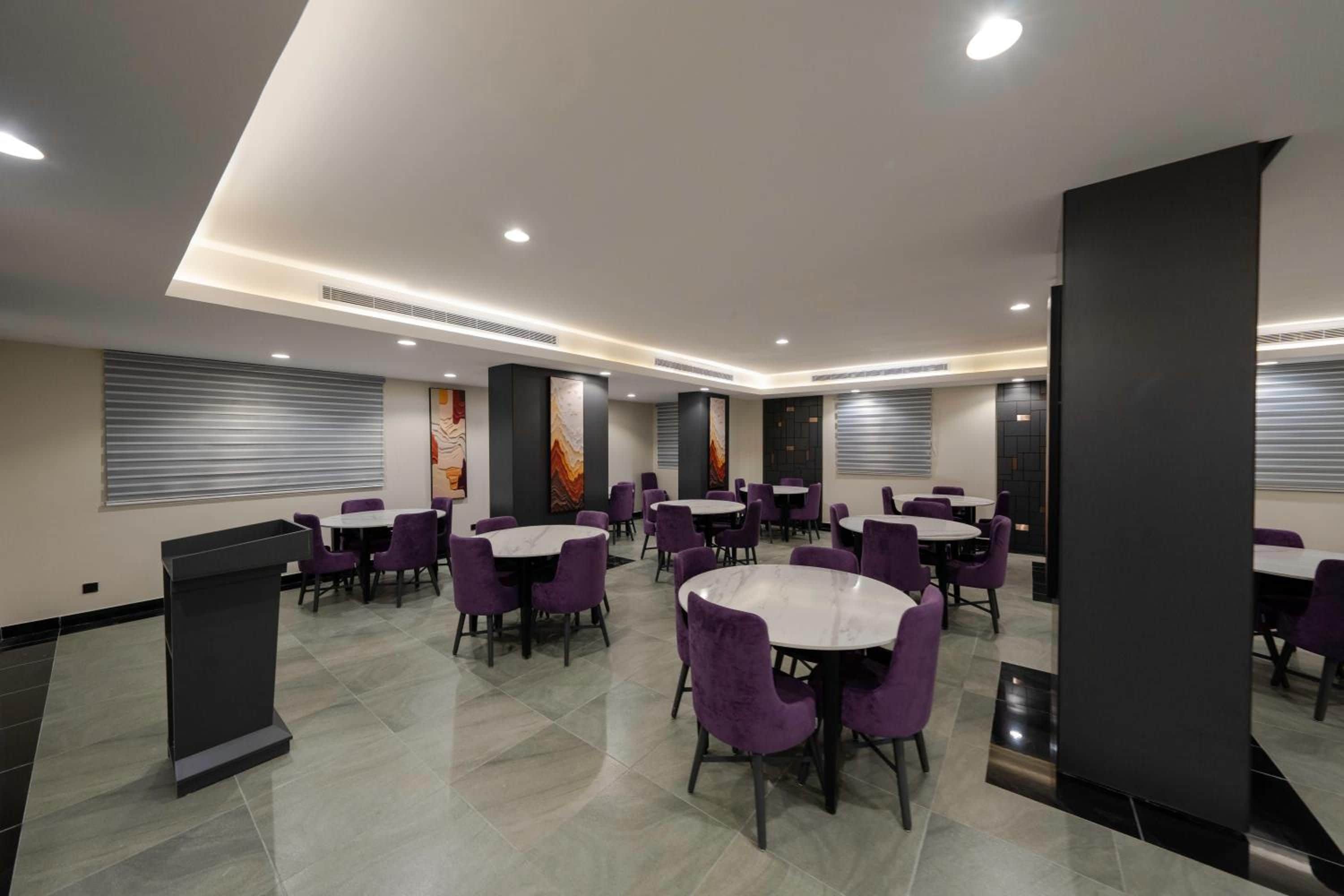 Un espace repas moderne avec des tables rondes et des chaises violettes, agrémenté d’une colonne centrale et d’œuvres d’art sur les murs.