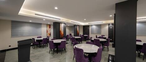 A modern dining area with round tables and purple chairs, featuring a central column and artwork on the walls.