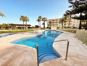 Une piscine dont le fond est recouvert de carreaux disposés selon un motif géométrique, entourée d’une terrasse en béton et de palmiers.