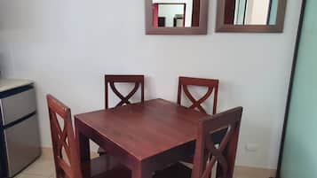 Un comedor con mesa de madera y cuatro sillas, un refrigerador y dos espejos fijados a la pared.