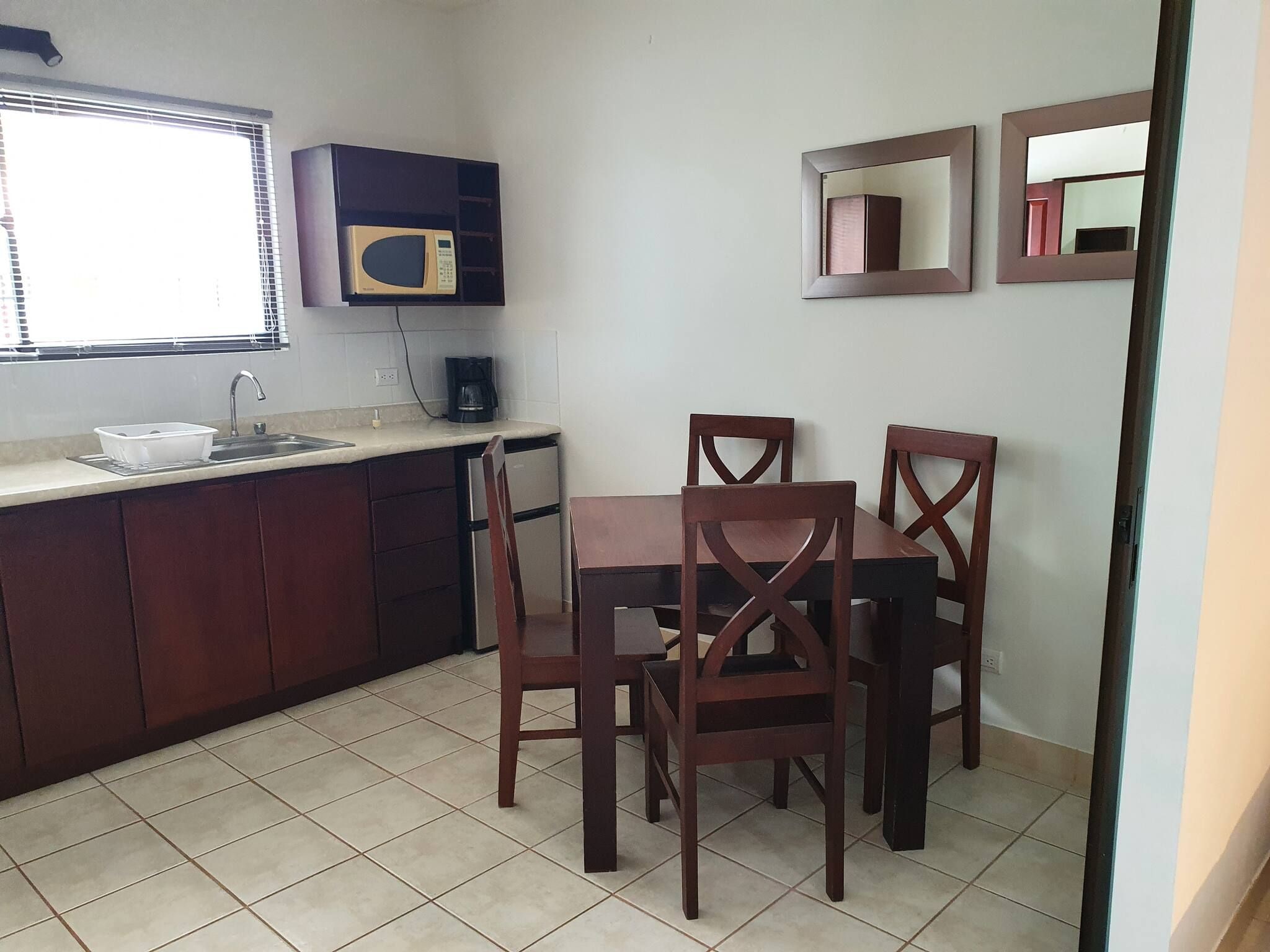 A compact kitchen with a microwave, sink, and a dining area with two chairs.