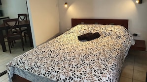 Een opgemaakt bed met een sprei met bladmotief, een donkerbruin kussen en twee wandlampen.