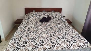 Una cama con colcha estampada de hojas, dos mesitas de noche y una mesilla.