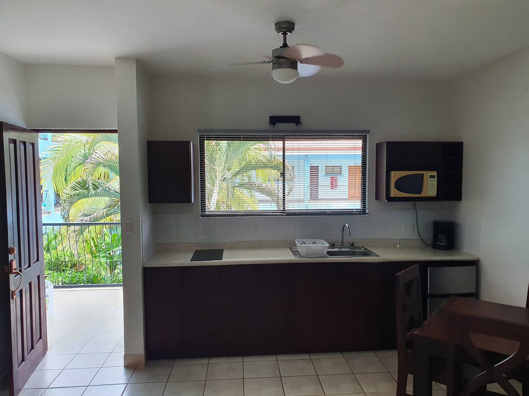 Una cocina compacta con ventana, ventilador de techo y microondas.