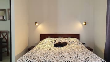 Una cama individual con una colcha estampada, dos lámparas fijadas a la pared, un cabecero de madera y un enchufe en la pared.