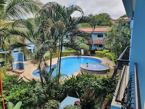 A swimming pool surrounded by lush greenery and a building with a tiled roof. - Marina Loft Studio # 207 (Sardinal)