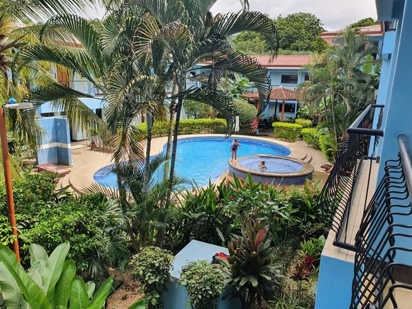 A pool surrounded by lush greenery and a blue building with a tiled roof. - Marina Loft Studio # 207 (Sardinal)
