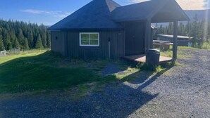 En træhytte med stort vindue, overdækket terrasse og grusvej.