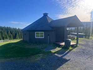 A wooden cabin with a large window, a covered outdoor area, and a gravel driveway. - Blafjell Hundesenter Fjellhotell (Vefsn)