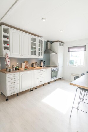 A modern kitchen with white cabinetry, a built-in oven, and a window with blinds. - Blafjell Hundesenter Fjellhotell (Vefsn)