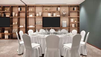 A conference room with a round table, white chairs, and a bookshelf with various items.