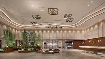 En rymlig entréhall med ett välvt tak, infälld belysning och en central sittgrupp med gröna soffor och bambuväxter.