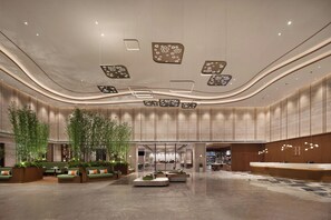 A spacious lobby with a curved ceiling, recessed lighting, and a central seating area with green sofas and bamboo plants. - Hilton Garden Inn Guiyang Gui'an New Area (Guiyang)