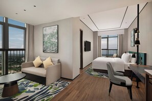 A hotel room with a bed, a sofa, a chair, a desk, and a large window offering a city view. - Hilton Garden Inn Guiyang Gui'an New Area (Guiyang)