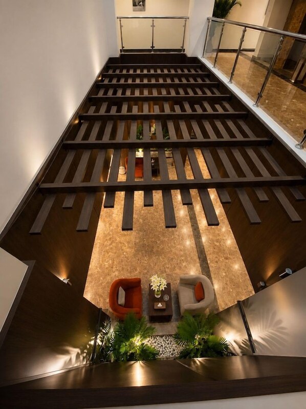 Una escalera moderna con barandilla de madera, una zona de estar con dos sillas y un pequeño arreglo de plantas en la parte inferior.