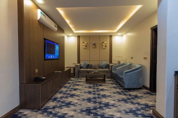 Un salon moderne avec un téléviseur à écran plat, un canapé, deux fauteuils, une table basse et un tapis à motifs.