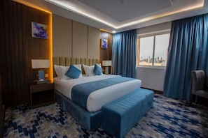 Une chambre d’hôtel avec un grand lit, une banquette, une table de chevet, une lampe, un tableau et une vue sur la ville.