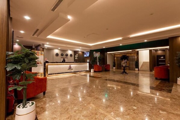 A hotel lobby with a reception desk, seating area, and a staircase leading to another floor.