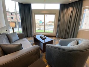 A modern hotel room with a large window, a sofa, a chair, and a coffee table.
