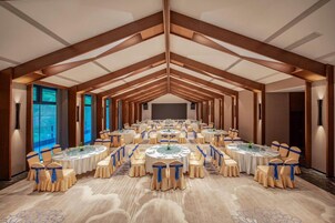 Un salón de conferencias con varias mesas redondas, cada una rodeada de sillas con cintas azules, preparado para una reunión o evento.
