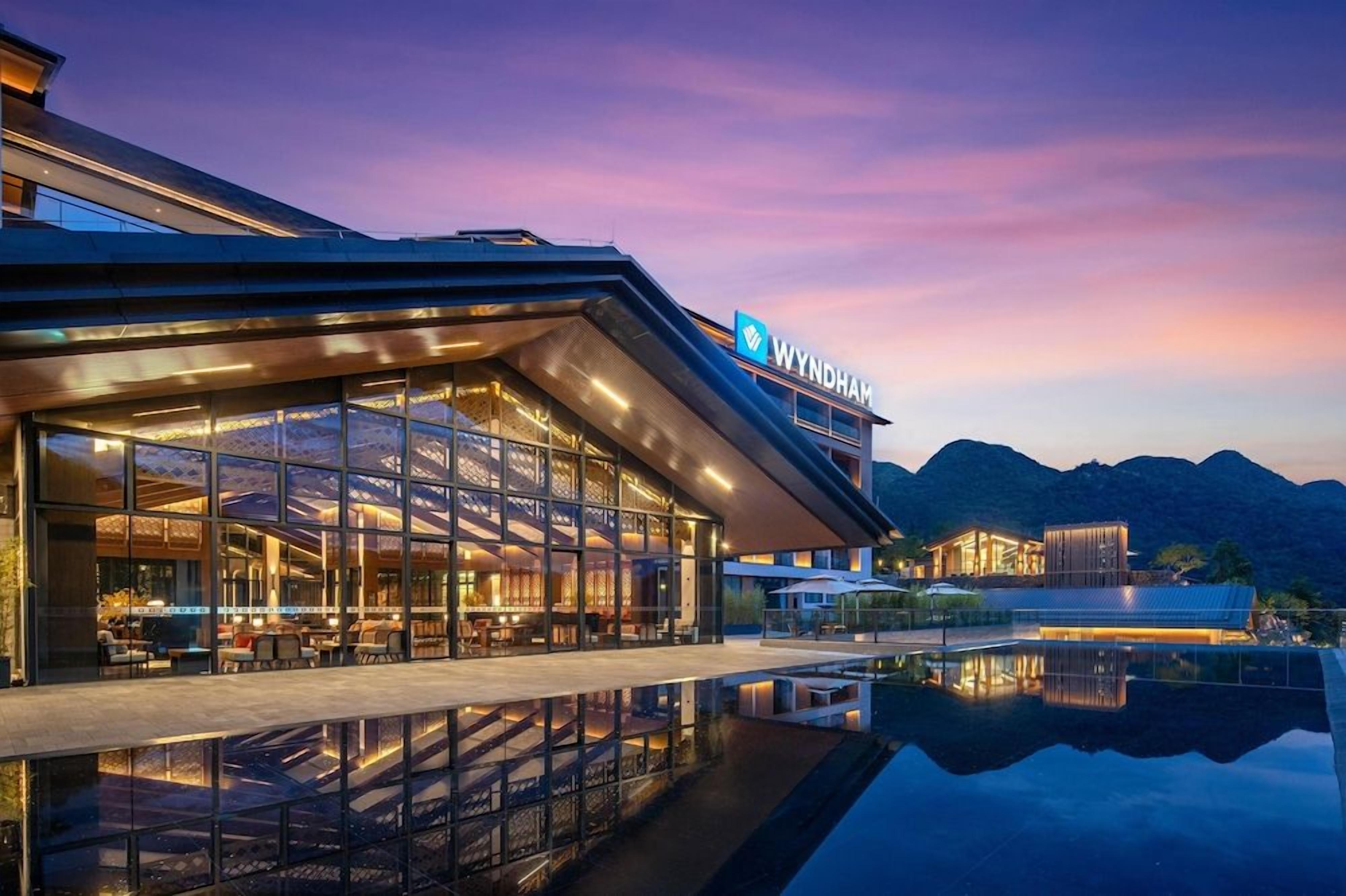 A modern hotel with a glass facade, outdoor seating, and a pool.