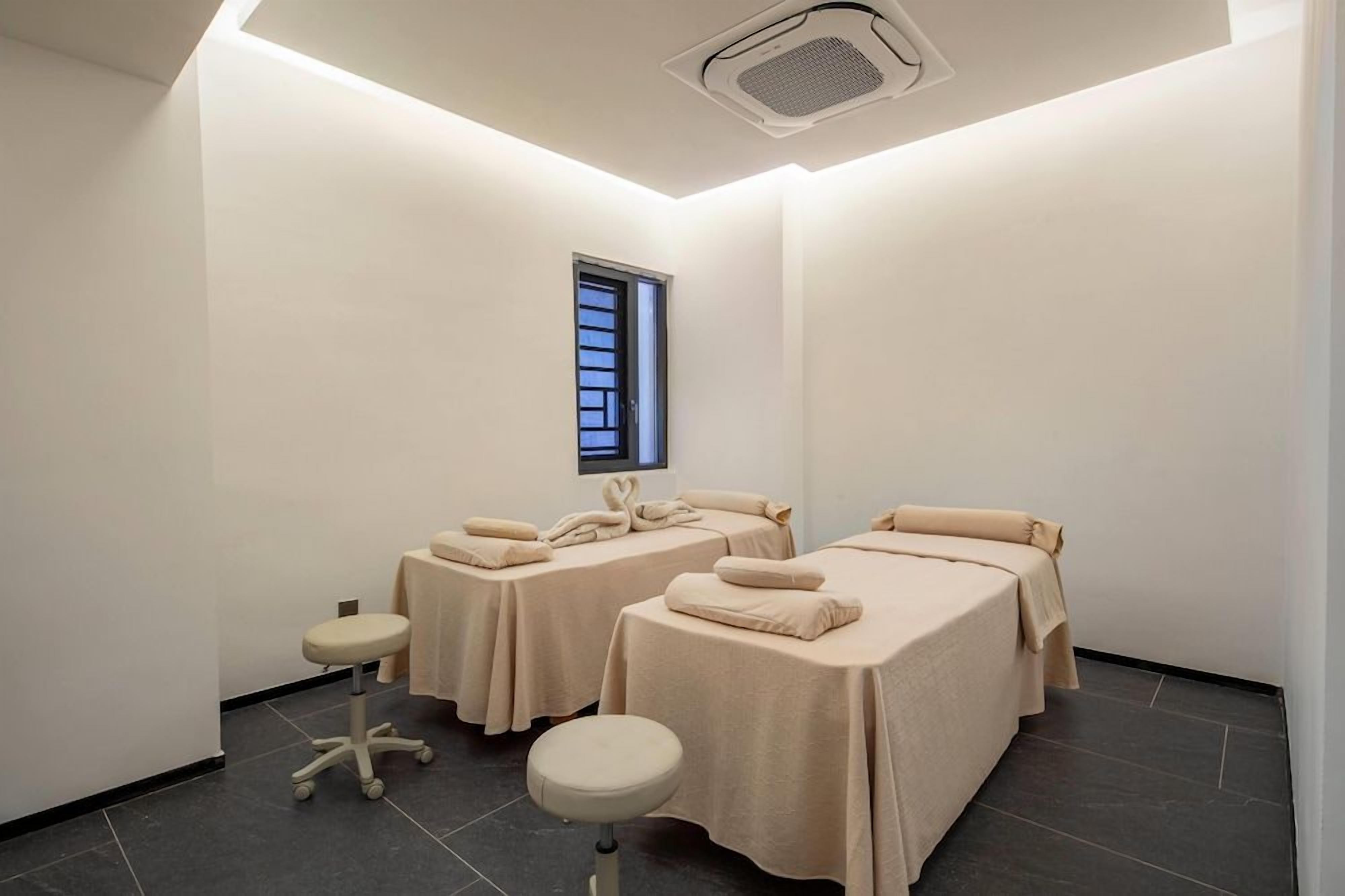 A spa room with two beds, a small stool, and a ceiling vent.