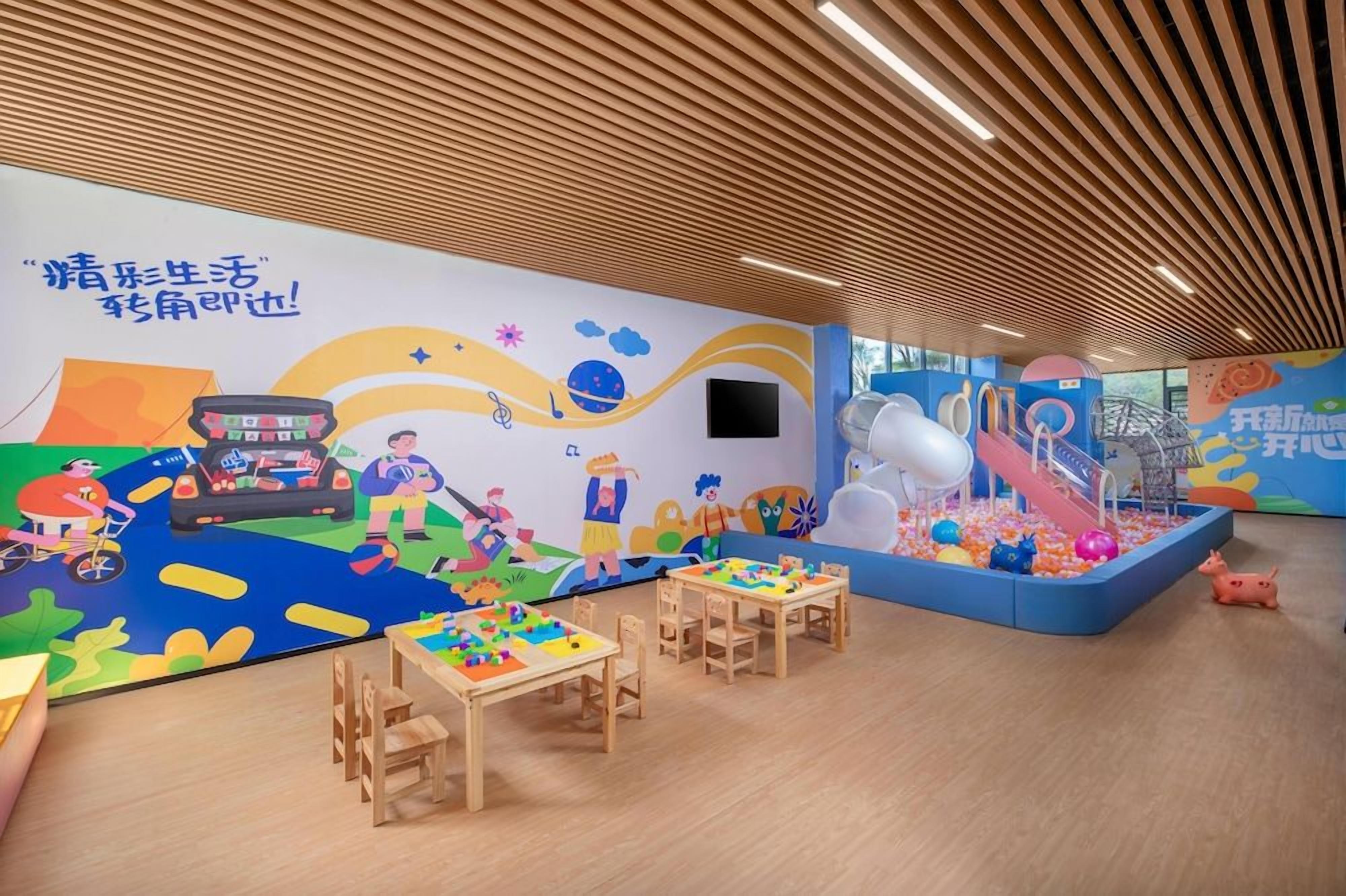 A children's play area with tables, chairs, a ball pit, and a mural on the wall.