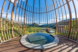 Un jacuzzi circular con cubierta de madera y barandilla metálica, rodeado de una vista panorámica de colinas y un lago.