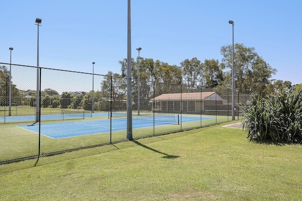 A fenced tennis court with floodlights, surrounded by grass and trees. - Reflections Holiday Parks Scotts Head (Scotts Head)